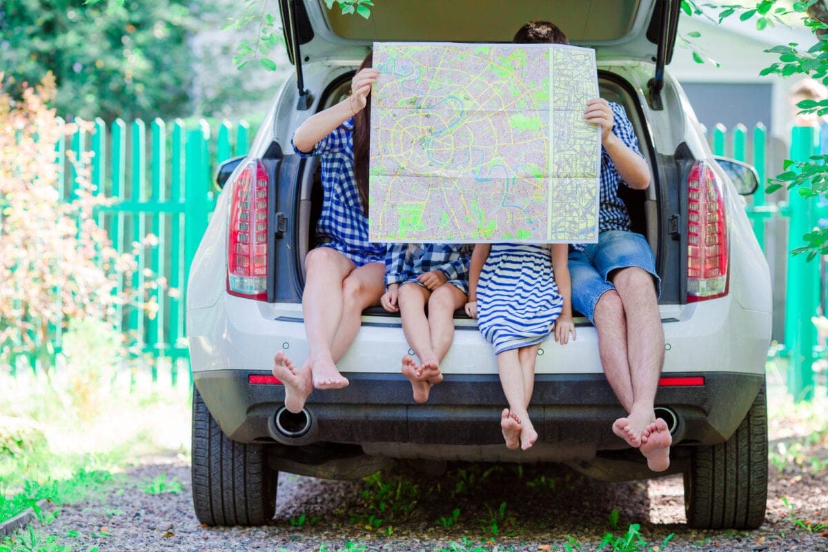 Family with two kids looking at map while traveling by car